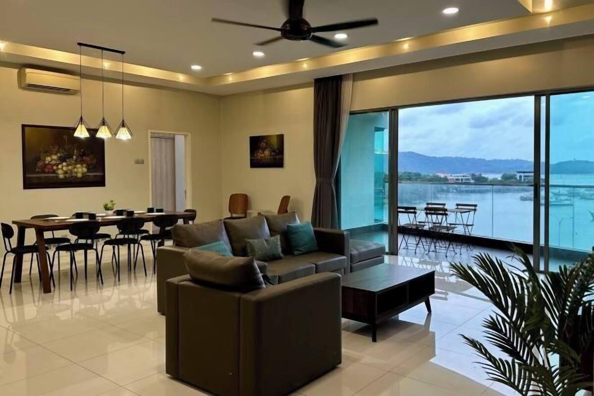 Una sala de estar moderna con sofá, mesa de centro, mesa de comedor y sillas. Hay un ventanal con vista a una masa de agua y montañas.