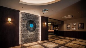 A hotel lobby with a brick wall, a circular artwork, and a reception desk. - ART HOTEL Sasebo Central (Sasebo)