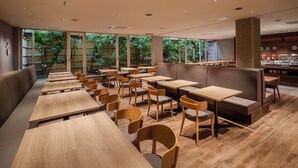 A restaurant with wooden tables and chairs, a bar area, and large windows with a view of greenery. - ART HOTEL Sasebo Central (Sasebo)