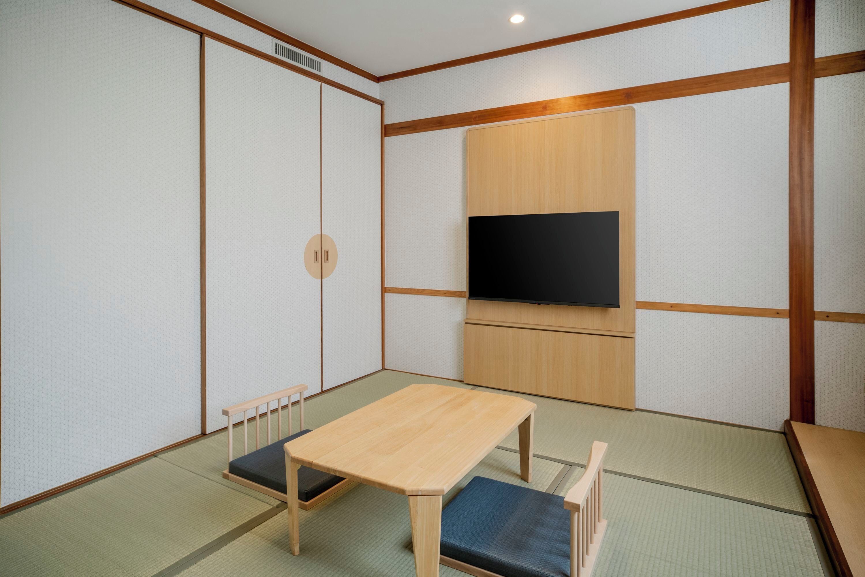 A traditional Japanese room with tatami flooring, a low wooden table, a TV mounted on the wall, and sliding shoji doors.