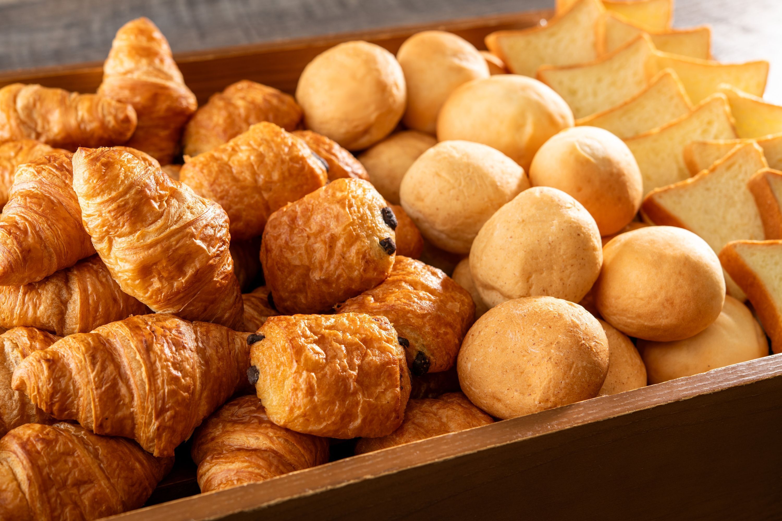 A wooden box filled with various types of bread and pastries.