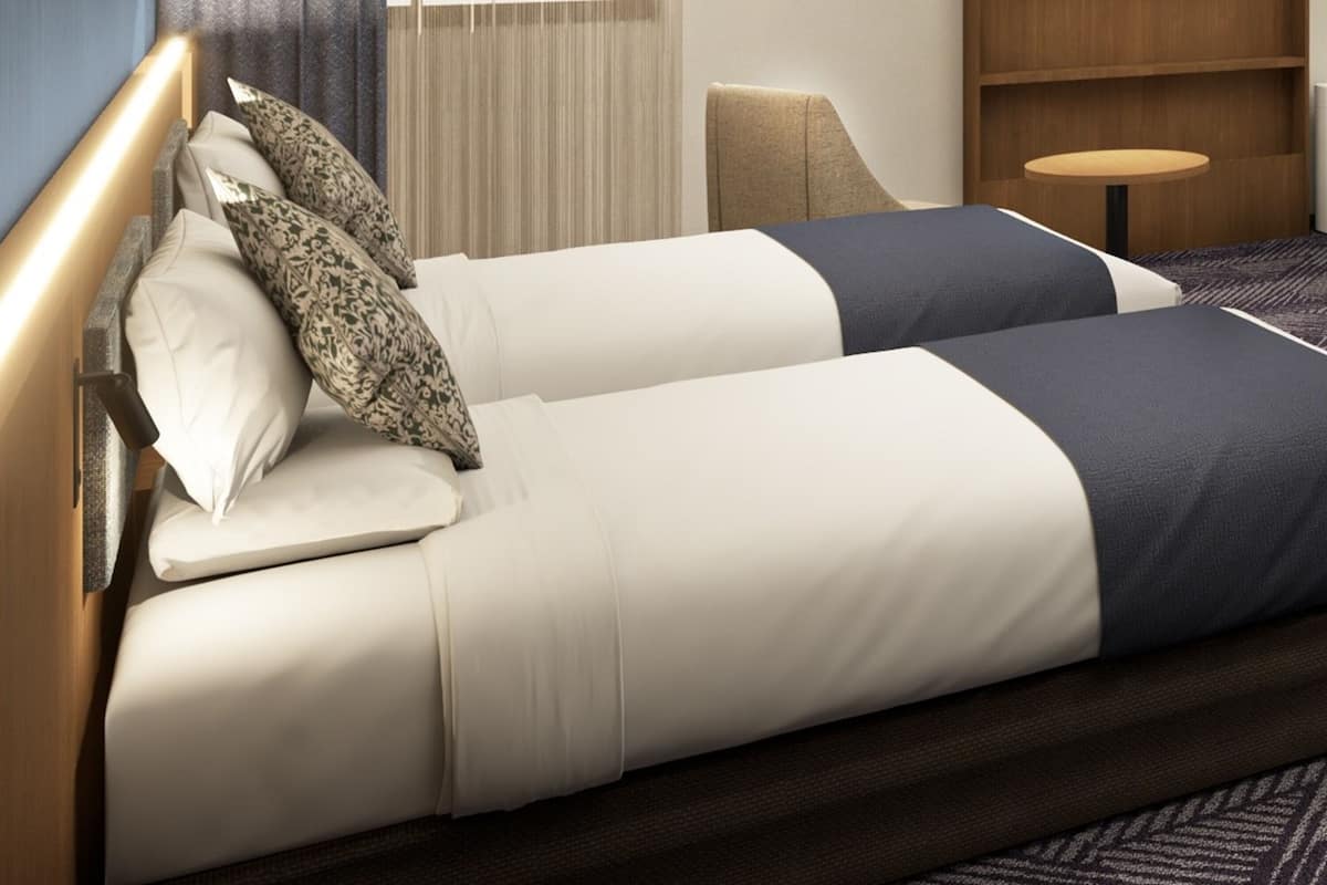 A hotel room with a bed, a chair, a small table, and a window with curtains.
