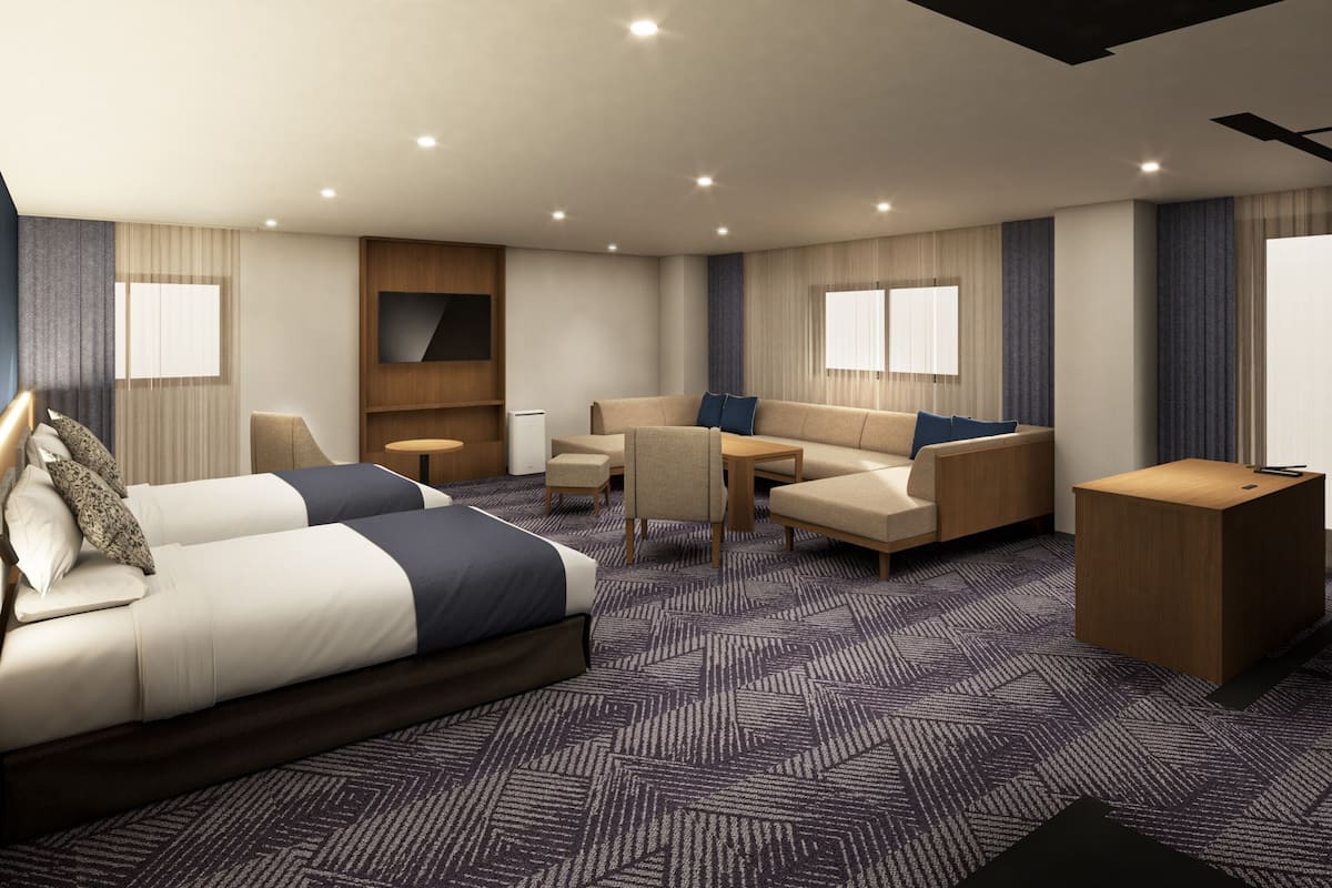 A hotel room with a bed, sofa, armchair, desk, and a TV mounted on the wall.