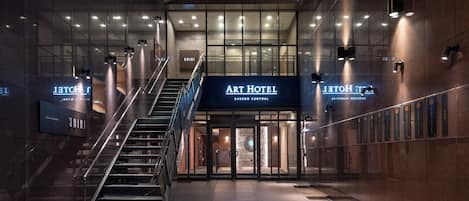Una entrada de hotel moderna con una escalera que lleva al vestíbulo, un letrero del Art Hotel y una zona de recepción.
