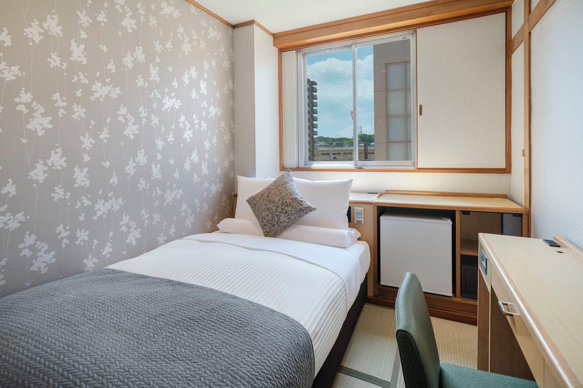 A hotel room with a bed, a desk, a chair, a window, and a view of buildings.