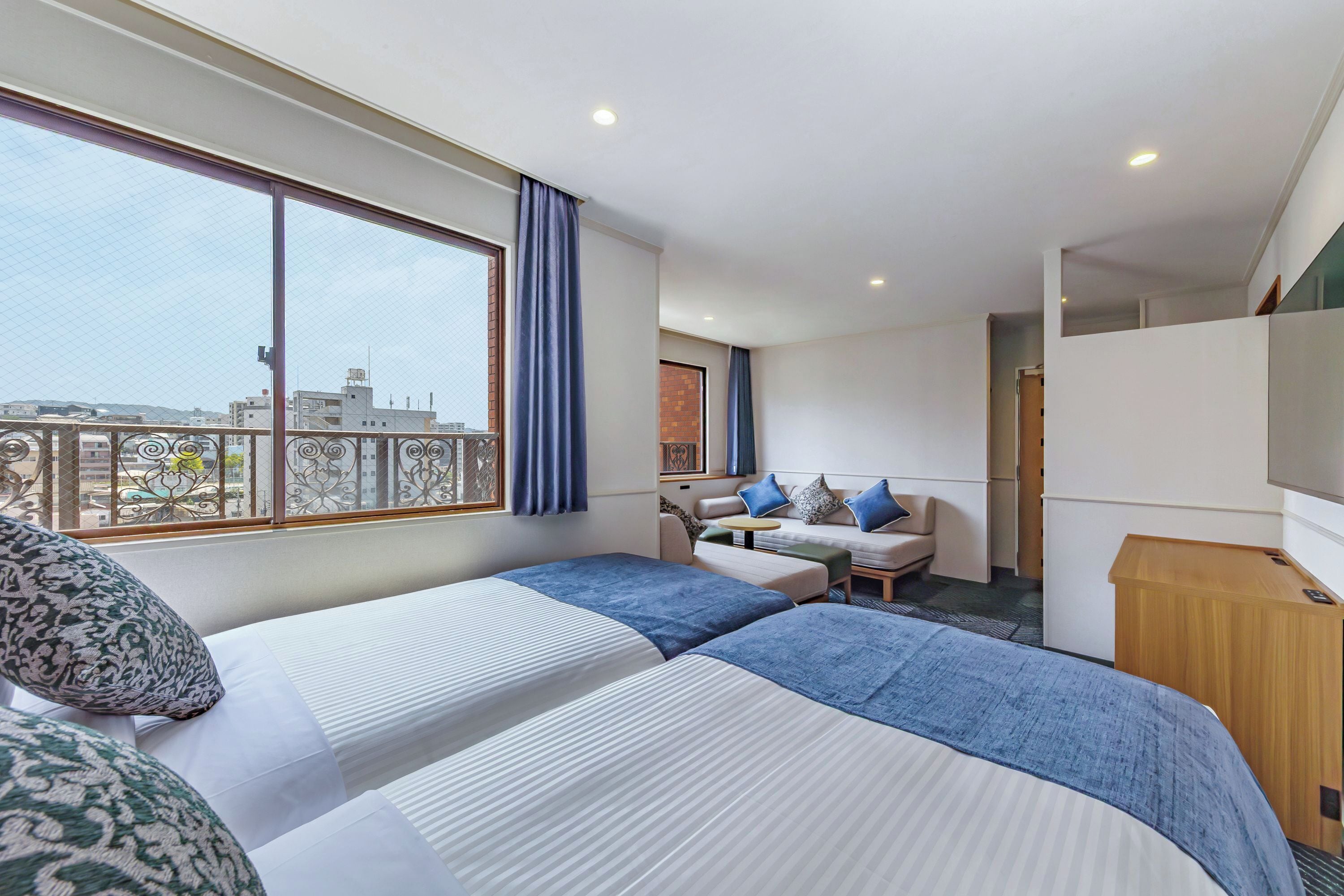 Habitación de hotel con dos camas, un sofá, una mesita y vistas a la ciudad.