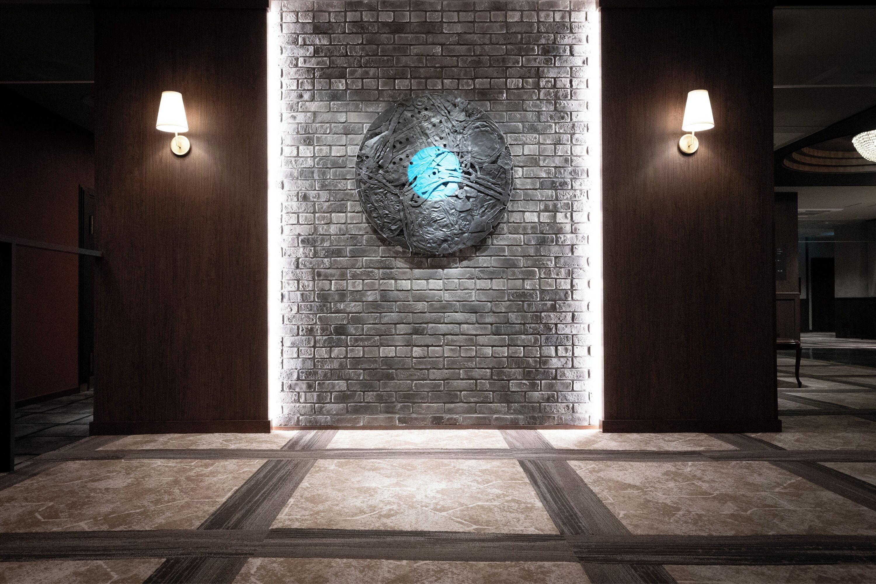 A hallway with a brick wall and a decorative metal piece. There are two wall-mounted lights on either side.