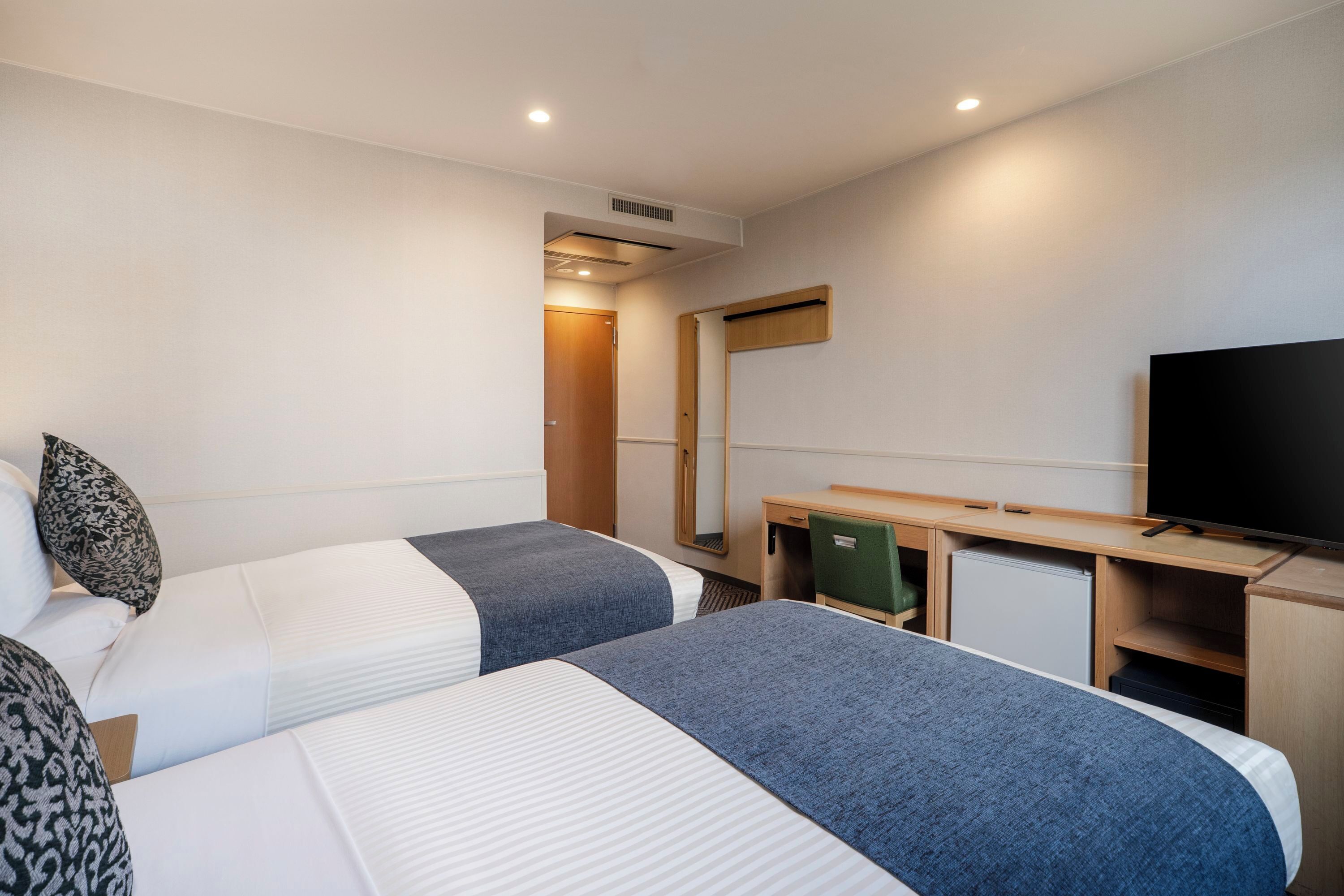 A hotel room with two beds, a desk, a television, and a mirror.