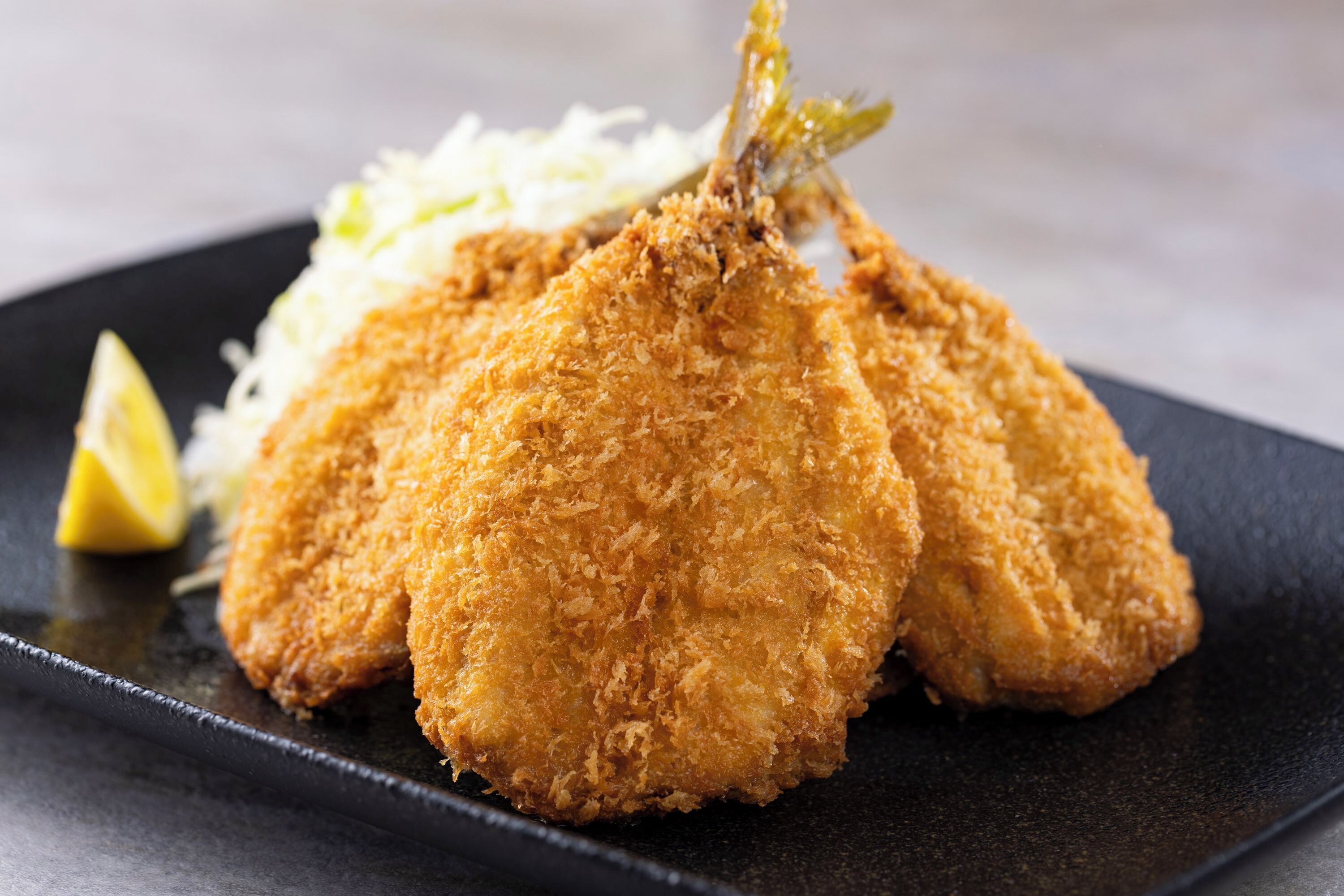 Ein Teller mit paniertem und frittiertem Essen, vermutlich Hähnchen, serviert mit Krautsalat und einem Zitronenschnitz.