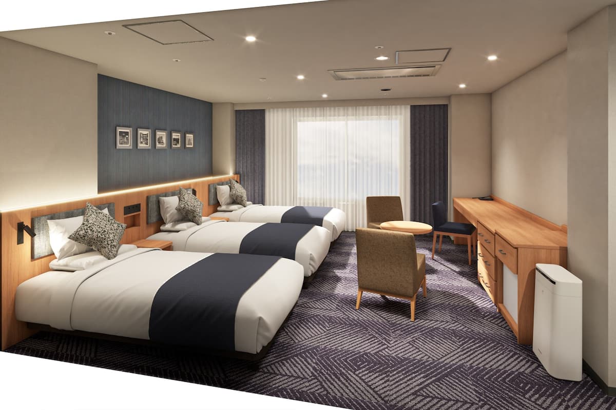 Habitación de hotel con dos camas, un escritorio, una silla, un radiador y un ventanal con cortinas.