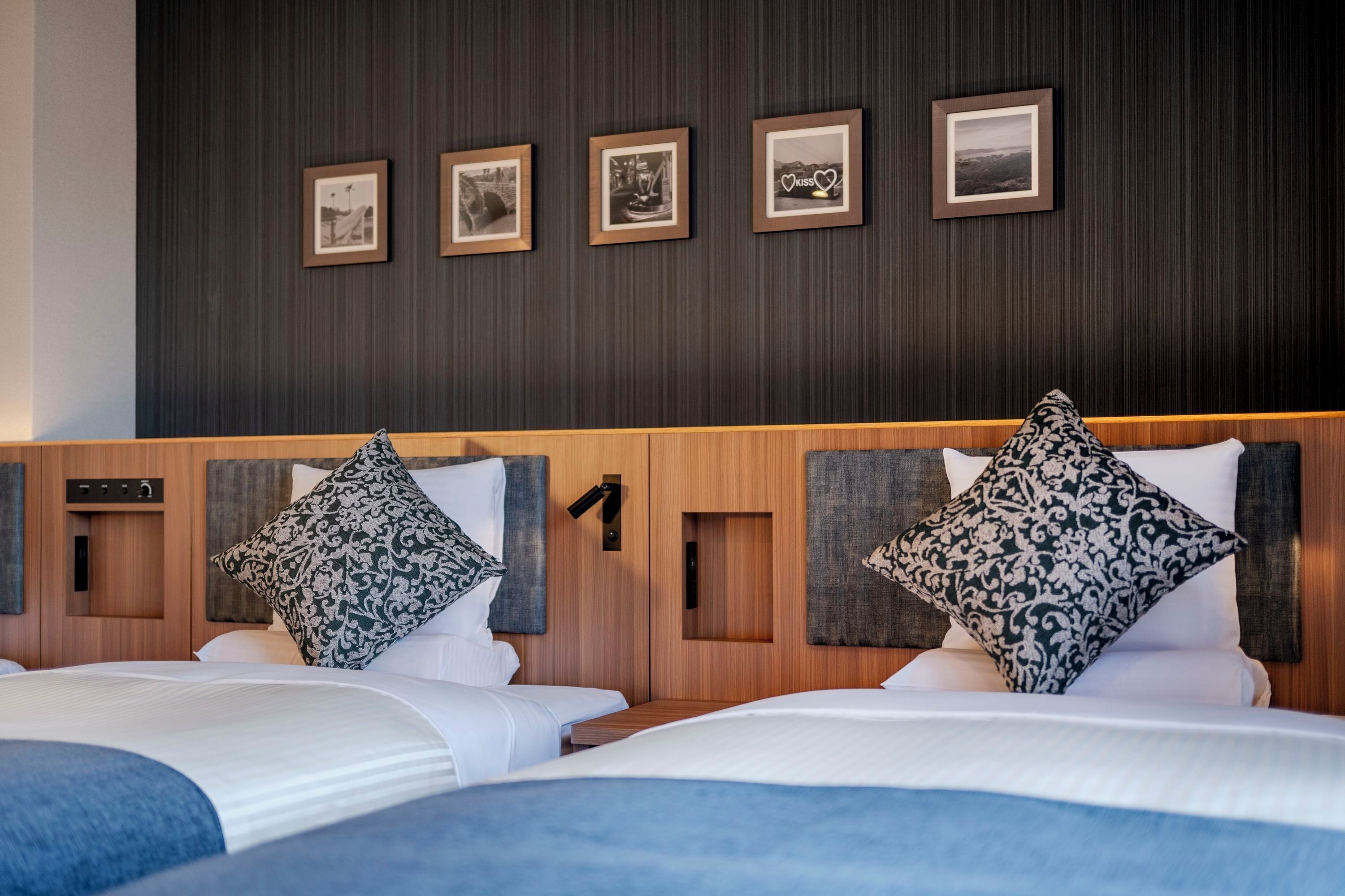 Ein Hotelzimmer mit zwei Betten, einem dunklen Holzkopfende und vier gerahmten Bildern an der Wand.