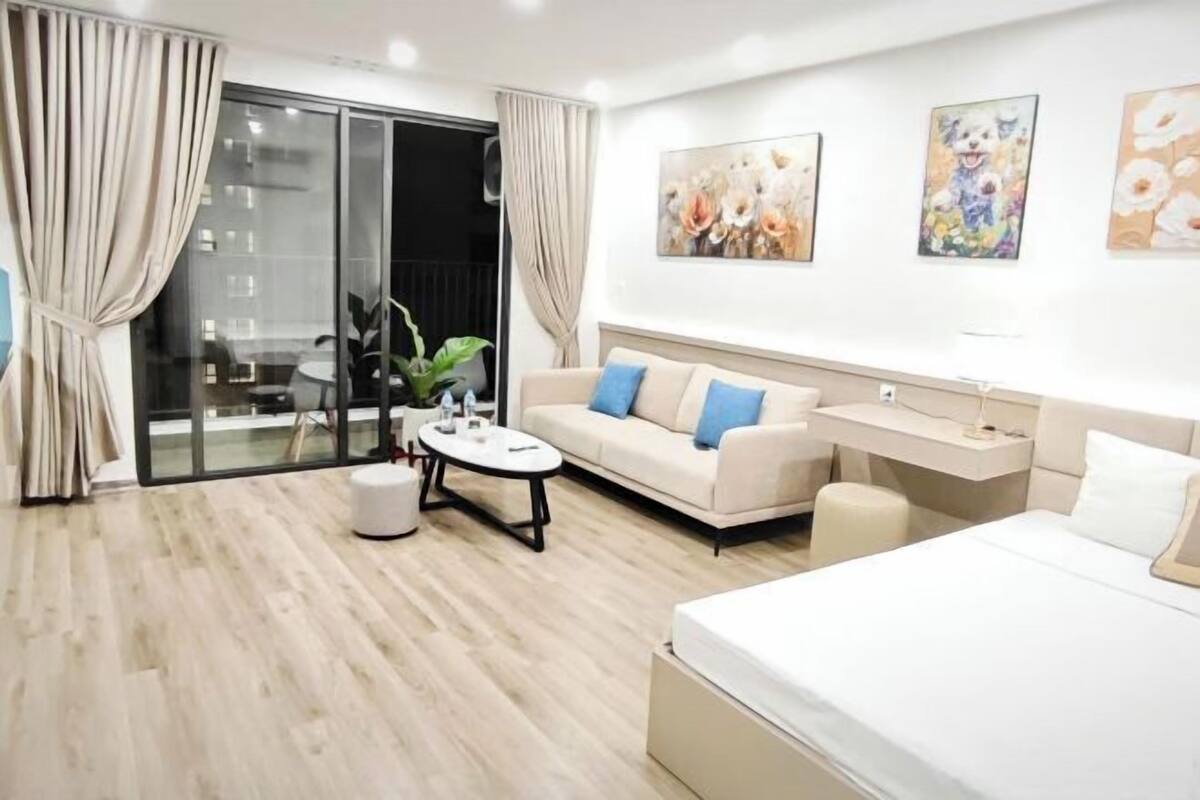 A modern hotel room with a sofa, a bed, a desk, and a sliding glass door leading to a balcony.
