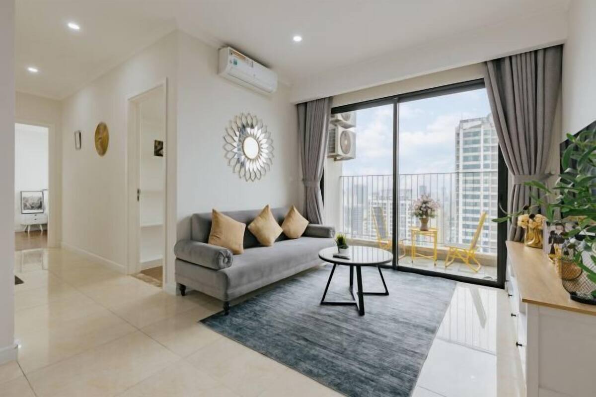 A modern living room with a grey sofa, a round coffee table, and a balcony with a view of the city.