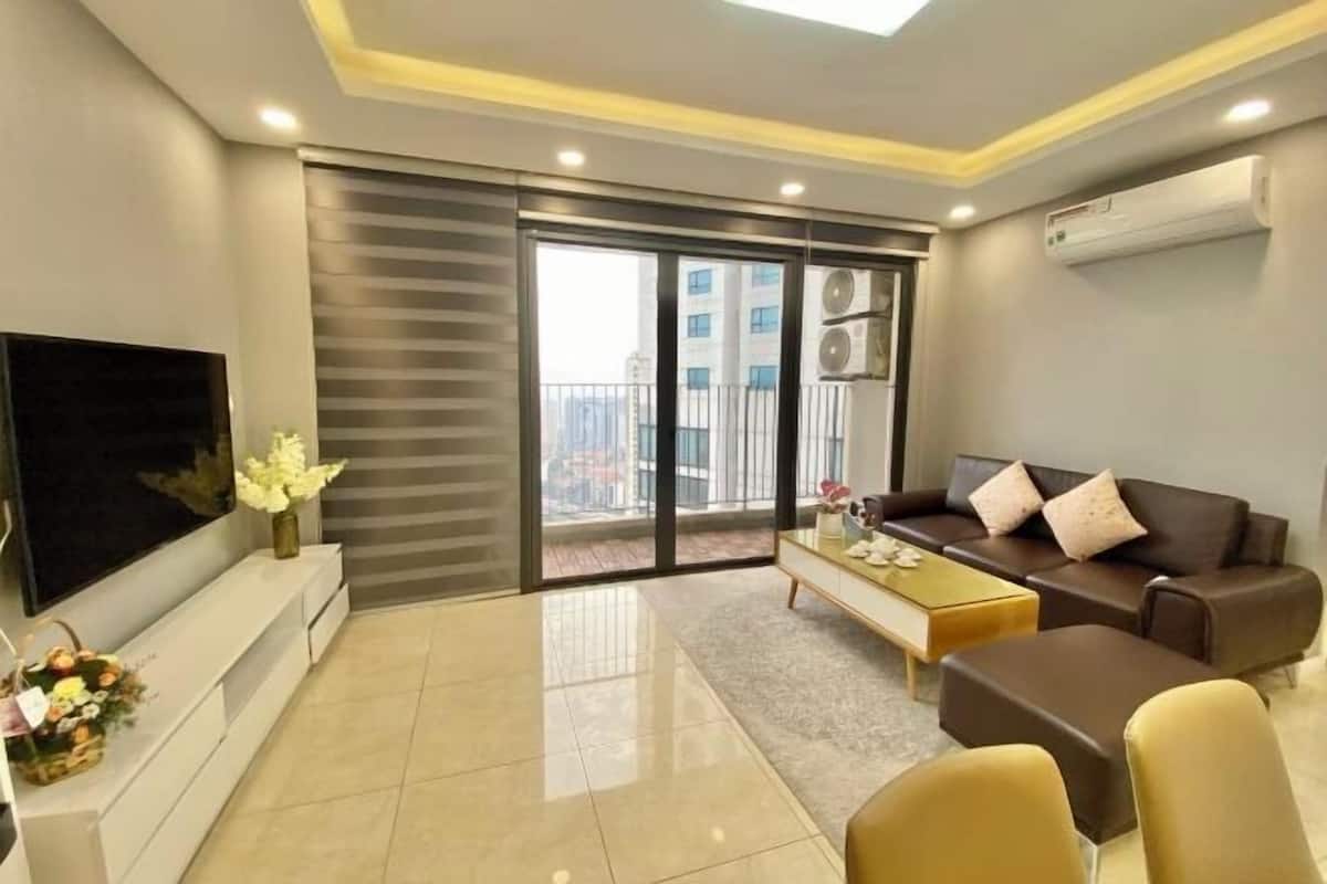 A modern living room with a flat-screen TV, a sofa set, a coffee table, and a sliding glass door leading to a balcony.