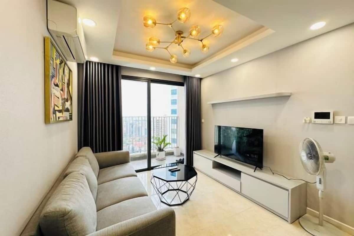 A modern living room with a sofa, a glass coffee table, a flat-screen TV, and a ceiling light fixture.