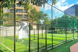 Un terrain de sport clôturé, doté d’un filet, entouré de verdure et de bâtiments.