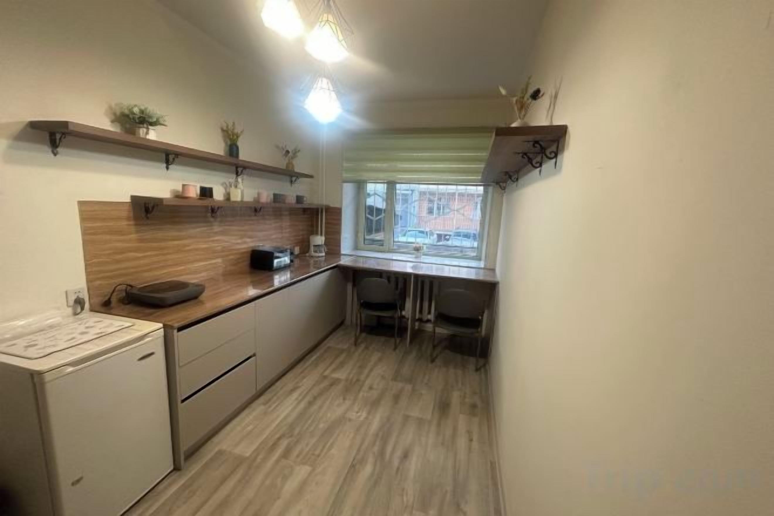 A compact kitchen with a refrigerator, a microwave, and a sink. There is a window with blinds and a small table with chairs.