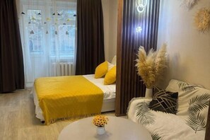 A bedroom with a bed, a bedside table with a vase of flowers, and a sofa with leaf-patterned cushions. - Ray apartment (Ulaanbaatar)