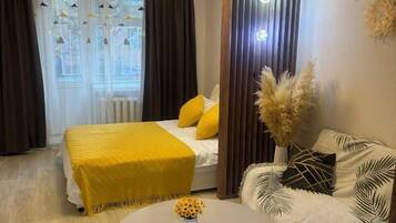 A hotel room with a bed, a sofa, a round table with a vase, and a window with curtains.