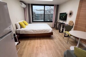 A hotel room with a bed, a desk, a chair, a TV, and a window. - Stay in JEJU (Jeju)