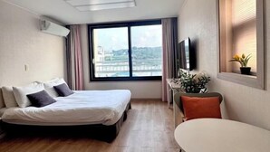Una camera d'albergo con un letto, una televisione, una finestra con tende e un tavolino con una pianta.