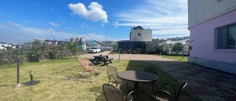 An outdoor patio with a table and chairs, a grassy area, and a building in the background.