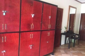 A room with a large red cabinet with multiple compartments, a small table with a chair, and a mirror on the wall. - Avila's Hostel Moalboal (Moalboal)