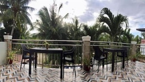A terrace with two tables and chairs, surrounded by palm trees and a patterned floor. - Avila's Hostel Moalboal (Moalboal)