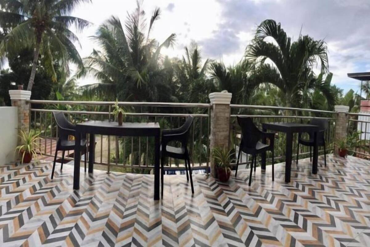 A terrace with two tables and chairs, surrounded by palm trees and a patterned floor.