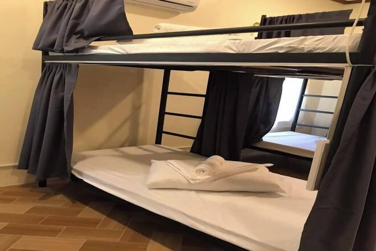 A bunk bed room with a window, curtains, and a wooden floor.