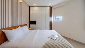 Habitación de hotel con una cama grande, cabecero de madera, luz fijada a la pared, ventana con vista a la ciudad y armario empotrado.