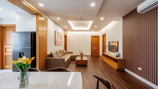 Una sala de estar moderna con comedor, piso de madera, una lámpara de techo y un televisor sobre un mueble de madera.