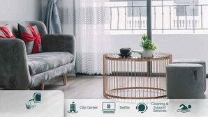 Ett modernt vardagsrum med en grå soffa, ett runt soffbord och utsikt över stadens centrum.