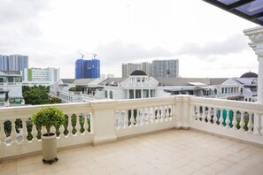 A balcony with a white balustrade, potted plants, and a view of surrounding buildings.