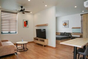 A modern living room with a flat-screen TV, a sofa, a dining table, and a ceiling fan.