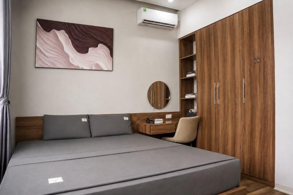 A bedroom with a bed, a desk, a chair, a wardrobe, and a wall-mounted air conditioner.