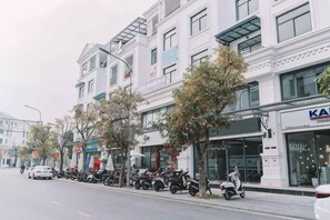 A street with buildings, parked scooters, and a car. - Merci Vinhomes Marina Hai Phong (Haiphong)