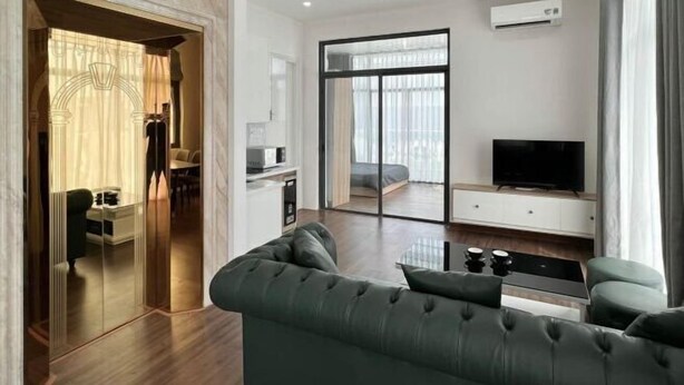 A modern living room with a sofa, a TV, and a glass door leading to a bedroom. - Merci Vinhomes Marina Hai Phong (Haiphong)