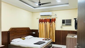 A bedroom with a wooden bed, an air conditioning unit, a ceiling fan, a wardrobe, and a small desk with a chair. - Hotel Rourkela Palace (Rourkela)