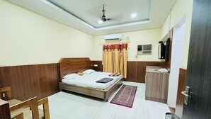 A bedroom with a bed, a desk, a chair, a wardrobe, an air conditioning unit, and a ceiling fan. - Hotel Rourkela Palace (Rourkela)