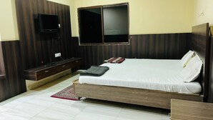 A bedroom with a bed, a TV mounted on the wall, a wooden bench, and a small table. - Hotel Rourkela Palace (Rourkela)