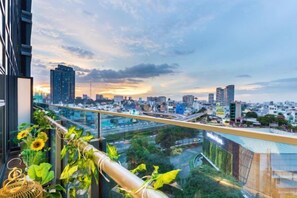 A cityscape view from a balcony with a glass railing, featuring modern buildings and a sunset. - An Corner - Sunwah Pearl Apartment (Ho Chi Minh City)