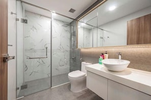 Une salle de bain moderne avec une douche à l’italienne en verre, des toilettes blanches et un grand miroir au-dessus d’un lavabo blanc doté d’un plan de travail beige.