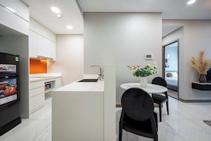 Une cuisine moderne avec des meubles blancs, un réfrigérateur noir et un petit îlot central doté d’un évier. On y trouve également un coin repas avec une table ronde et des chaises noires.