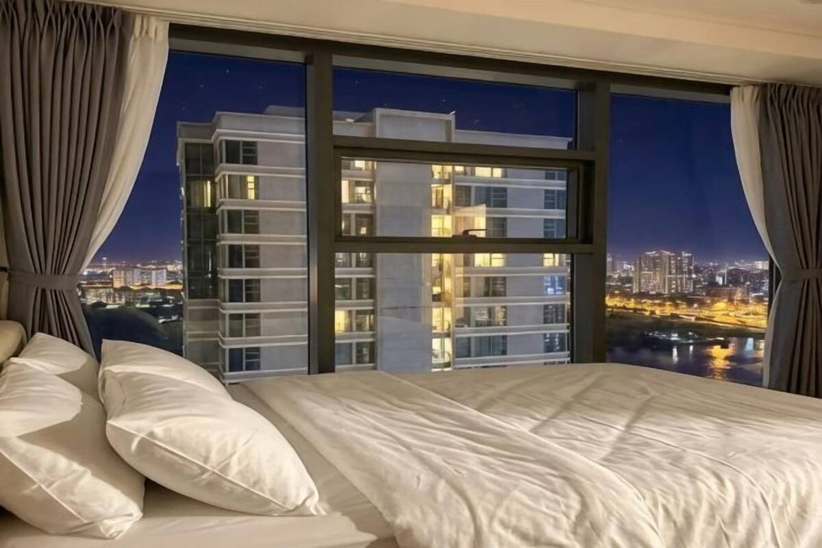 A hotel room with a large bed, a view of a cityscape, and a window with curtains.