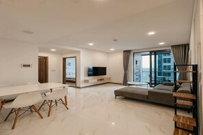 A modern living room with a dining table, sofa, TV, and large windows.