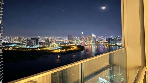 A night view of a city skyline with a river, illuminated buildings, and a moon in the sky. - An Corner - Sunwah Pearl Apartment (Ho Chi Minh City)