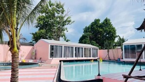 A swimming pool with a pink and white tiled deck, a palm tree, and a building with large windows.