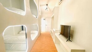 A modern hotel corridor with a wooden floor, white walls, and a flat-screen TV mounted on the wall.