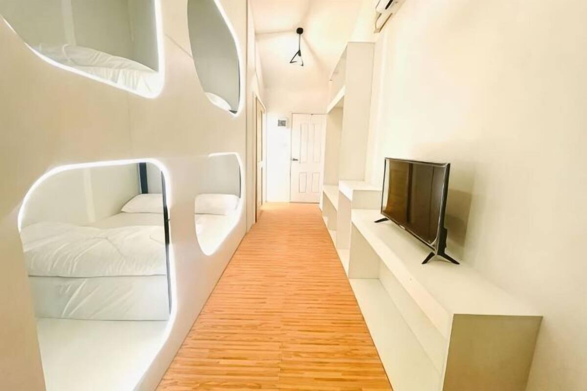 A modern hotel corridor with a wooden floor, white walls, and a flat-screen TV mounted on the wall.